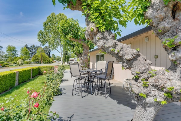 A patio with a table and chairs, surrounded by a garden with roses and a large tree.
