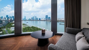 Ein modernes Zimmer mit großem Fenster, einem runden Tisch und einem grauen Sofa.