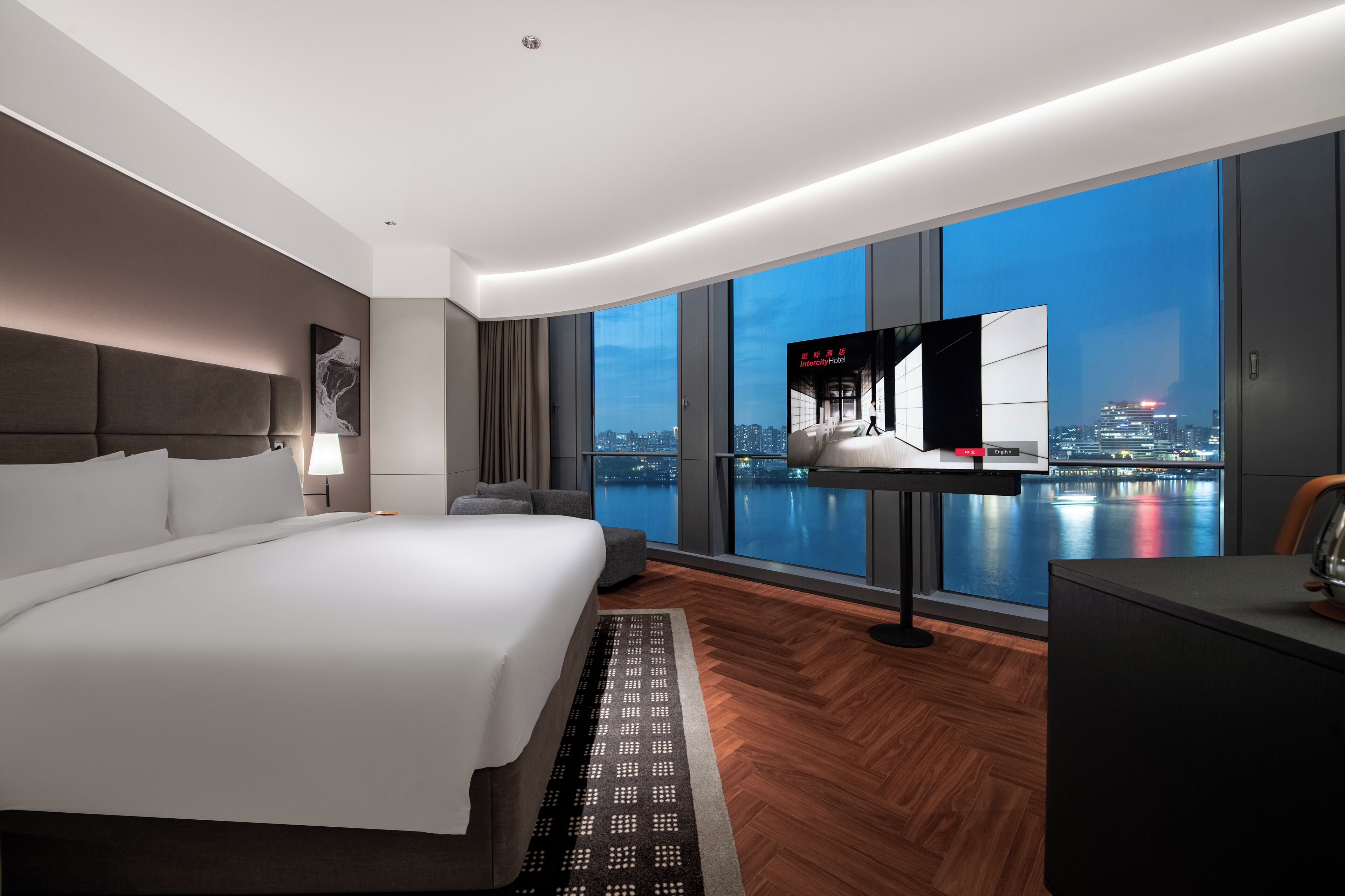 A modern hotel room with a large bed, a desk, a TV, and a city view.