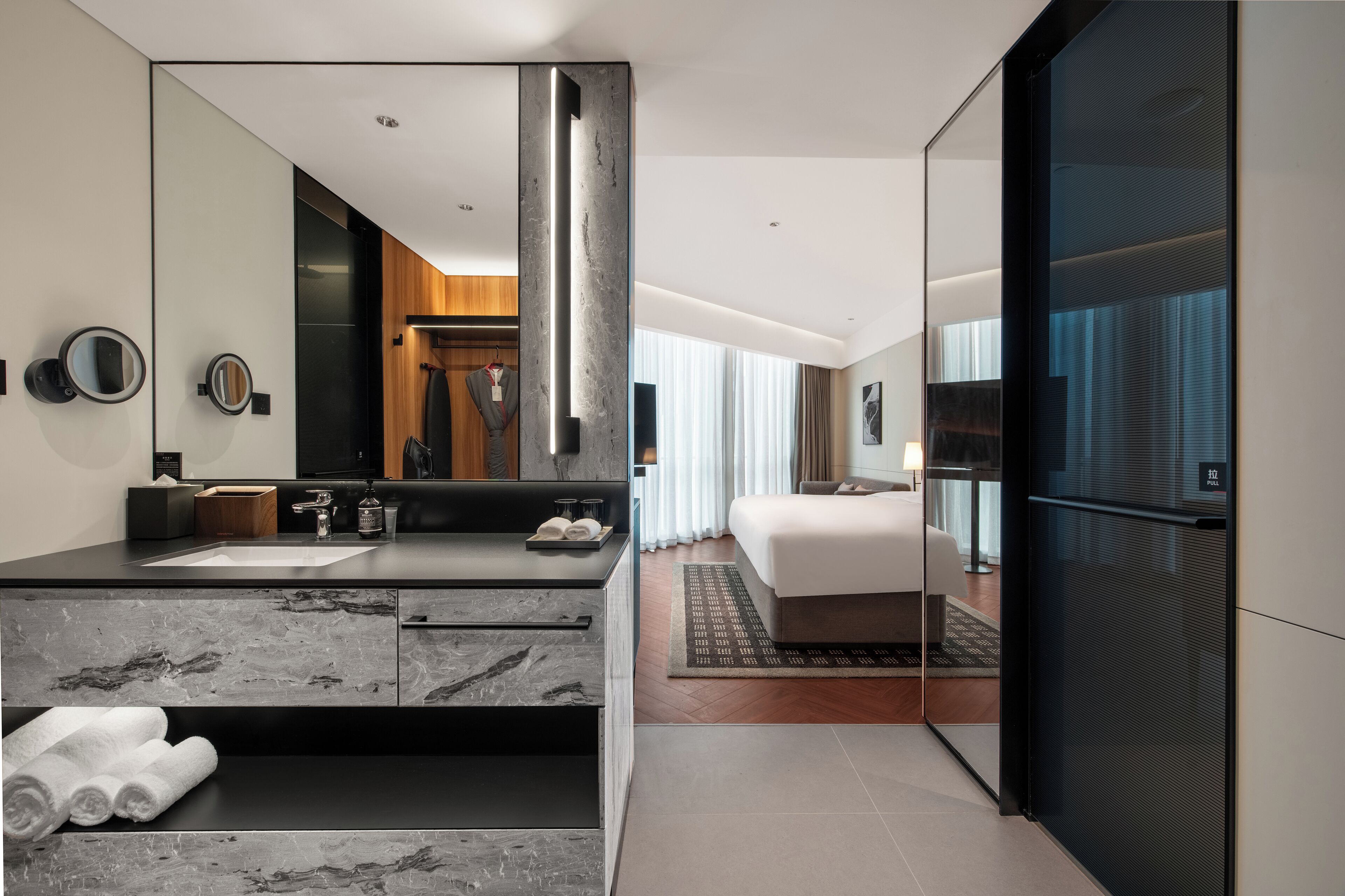 A modern hotel room with a large mirror, a marble vanity, a bed, and a sliding door to a balcony.