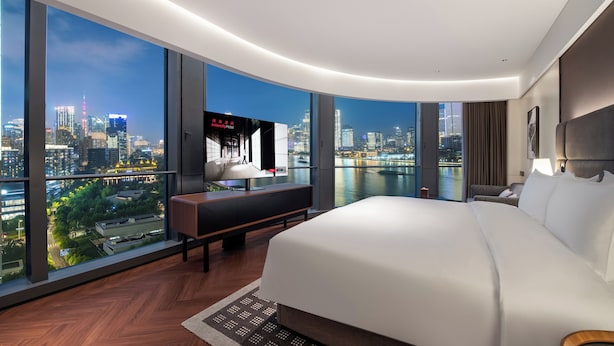 Ein modernes Hotelzimmer mit einem großen Bett, einem Schreibtisch mit Fernseher und Blick auf die Stadt.