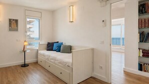 Ein Schlafzimmer mit Bett, Nachttisch, Lampe, Bücherregal und einem Fenster mit Aussicht.
