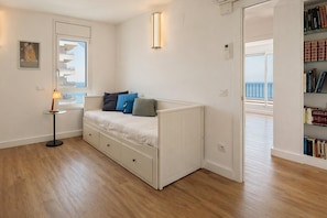 Ein Schlafzimmer mit Bett, Nachttisch, Lampe, Bücherregal und einem Fenster mit Aussicht.