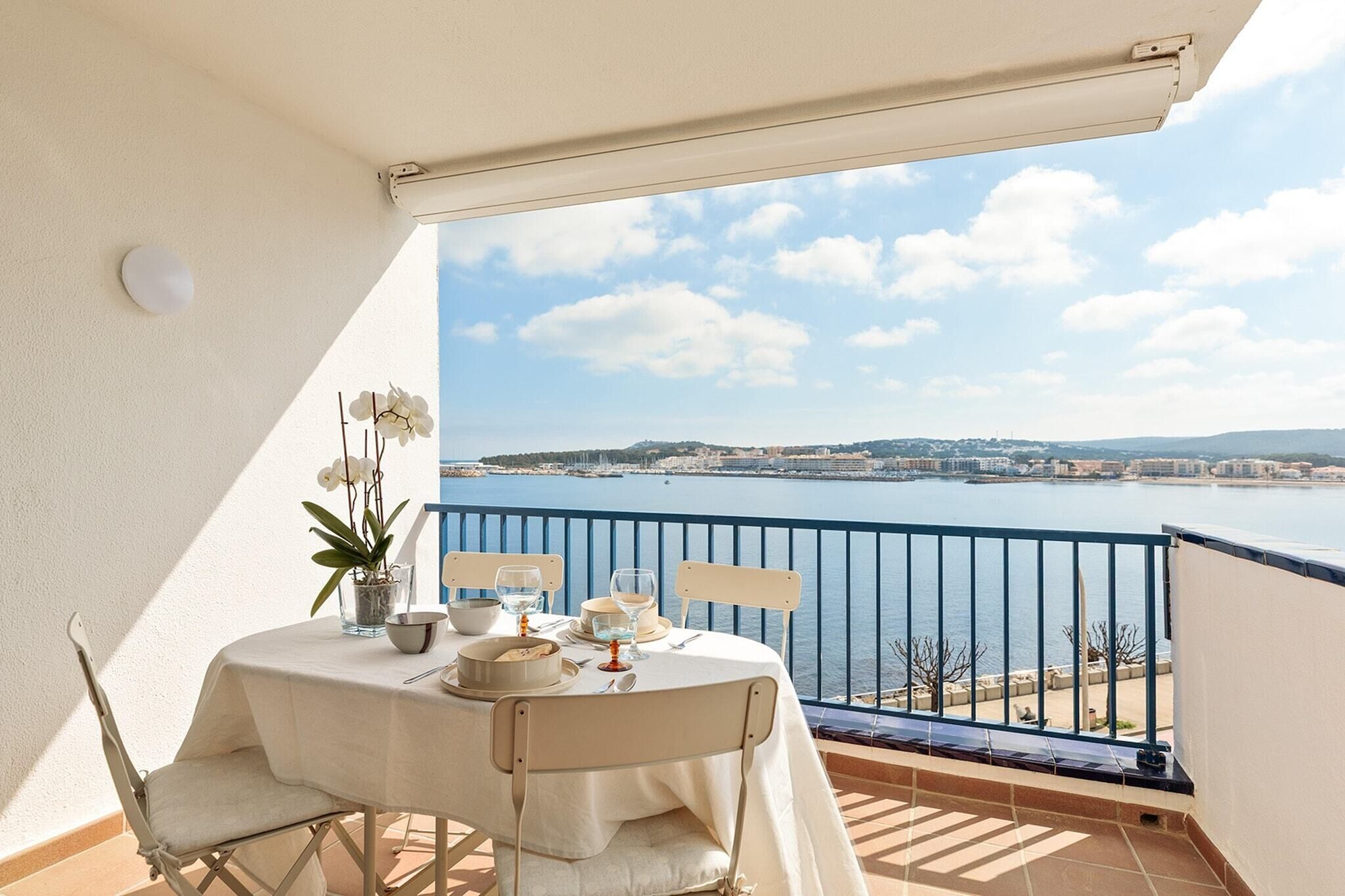 Ein Balkon mit Tisch für zwei Personen, mit Blick auf ein Gewässer und eine entfernte Landschaft.