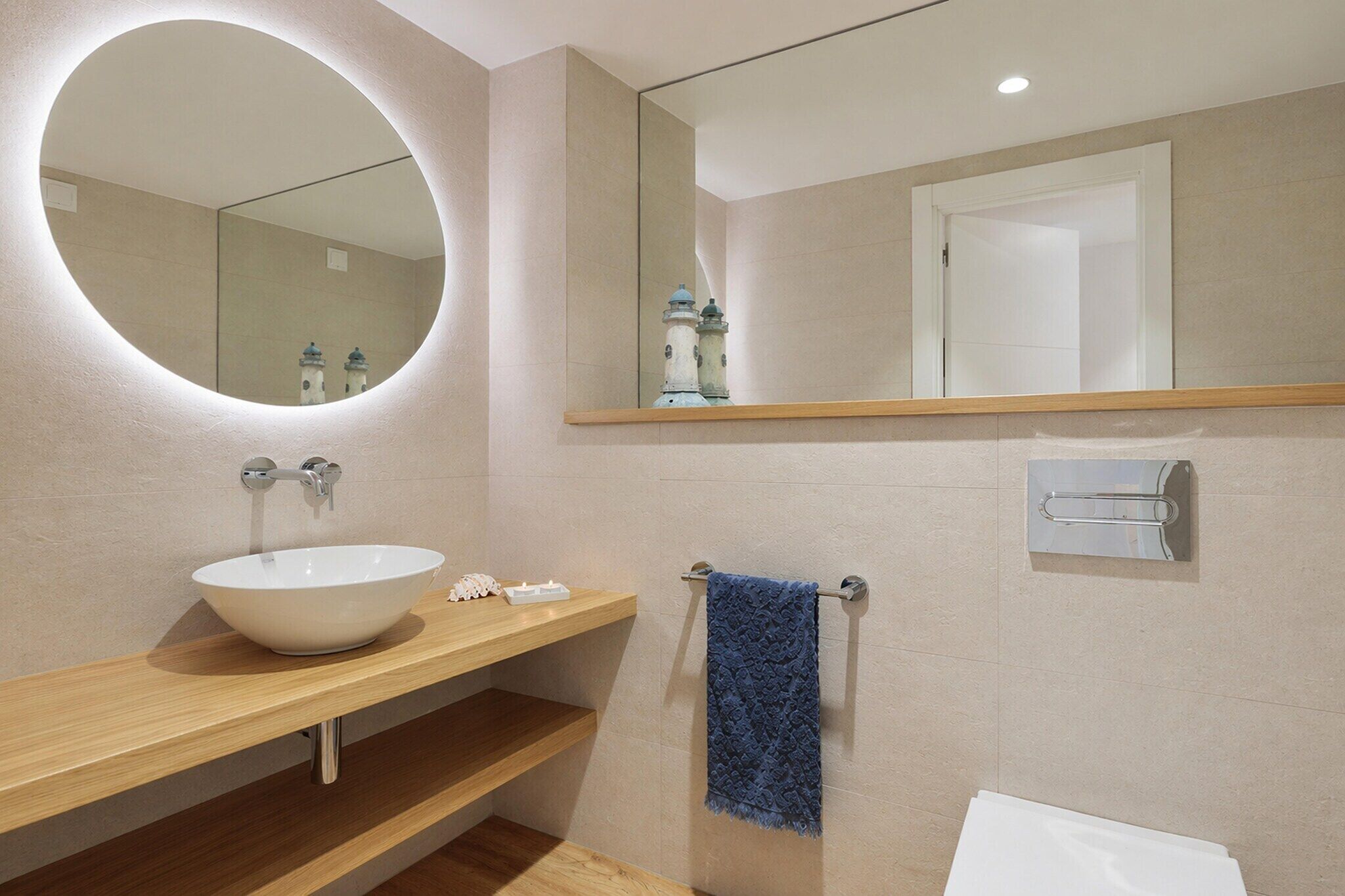 A bathroom with a round mirror, a white sink, wooden shelves, a towel rack, and a towel.