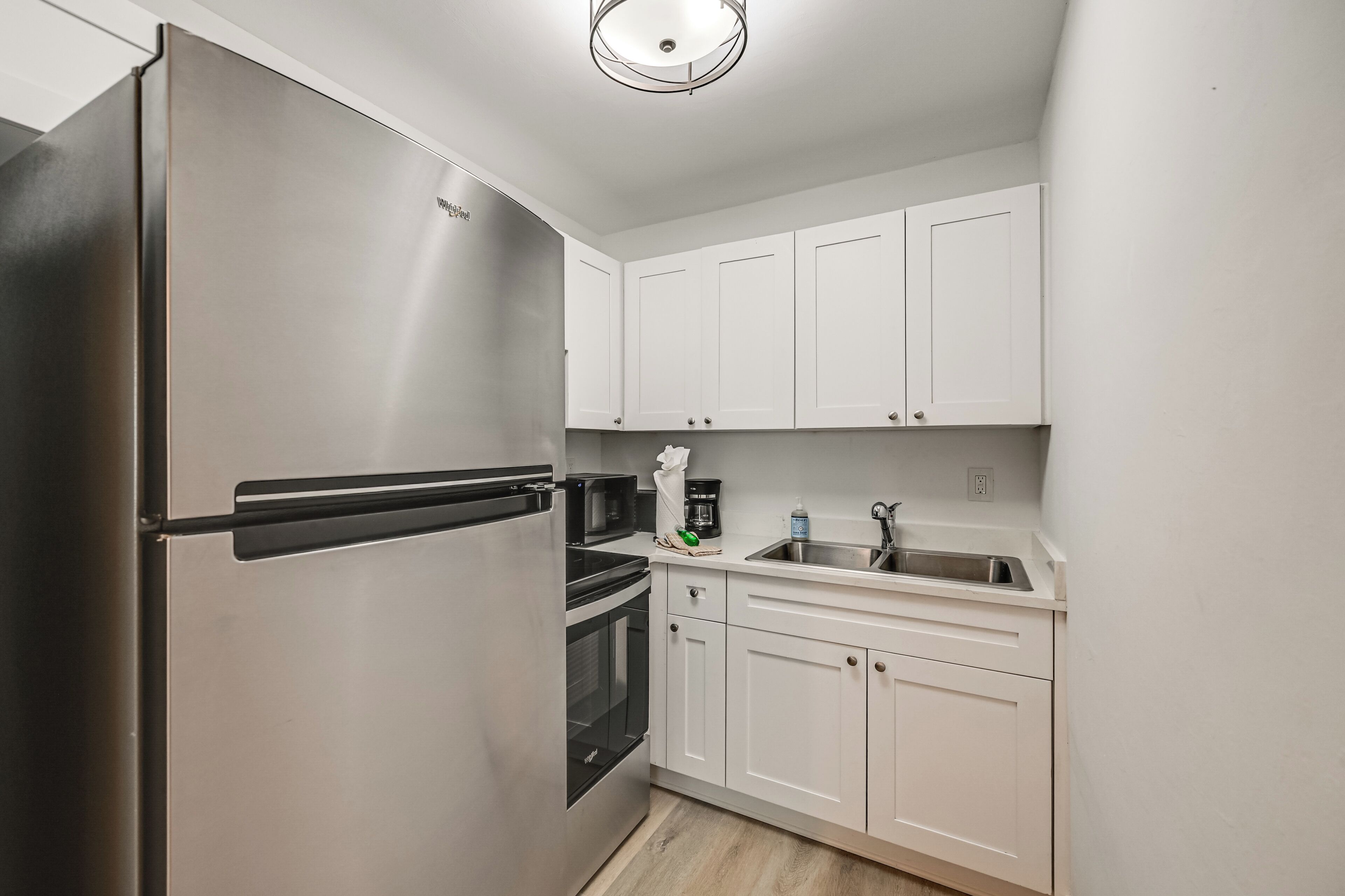 A compact kitchen with white cabinets, a stainless steel refrigerator, a microwave, a coffee maker, and a sink.