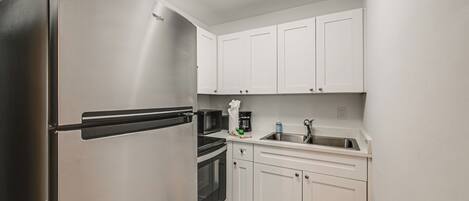 A compact kitchen with white cabinets, a stainless steel refrigerator, a microwave, a coffee maker, and a sink.