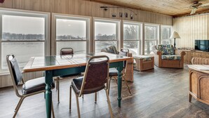 A dining area with a table and chairs, large windows, a ceiling fan, and a television. - Lakefront Home w/ Views, 7 Mi to Dtwn Paw Paw (Paw Paw)