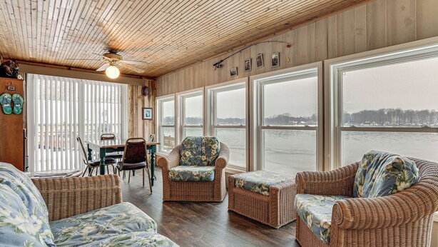A room with wicker furniture, large windows, a ceiling fan, and a view of a body of water. - Lakefront Home w/ Views, 7 Mi to Dtwn Paw Paw (Paw Paw)