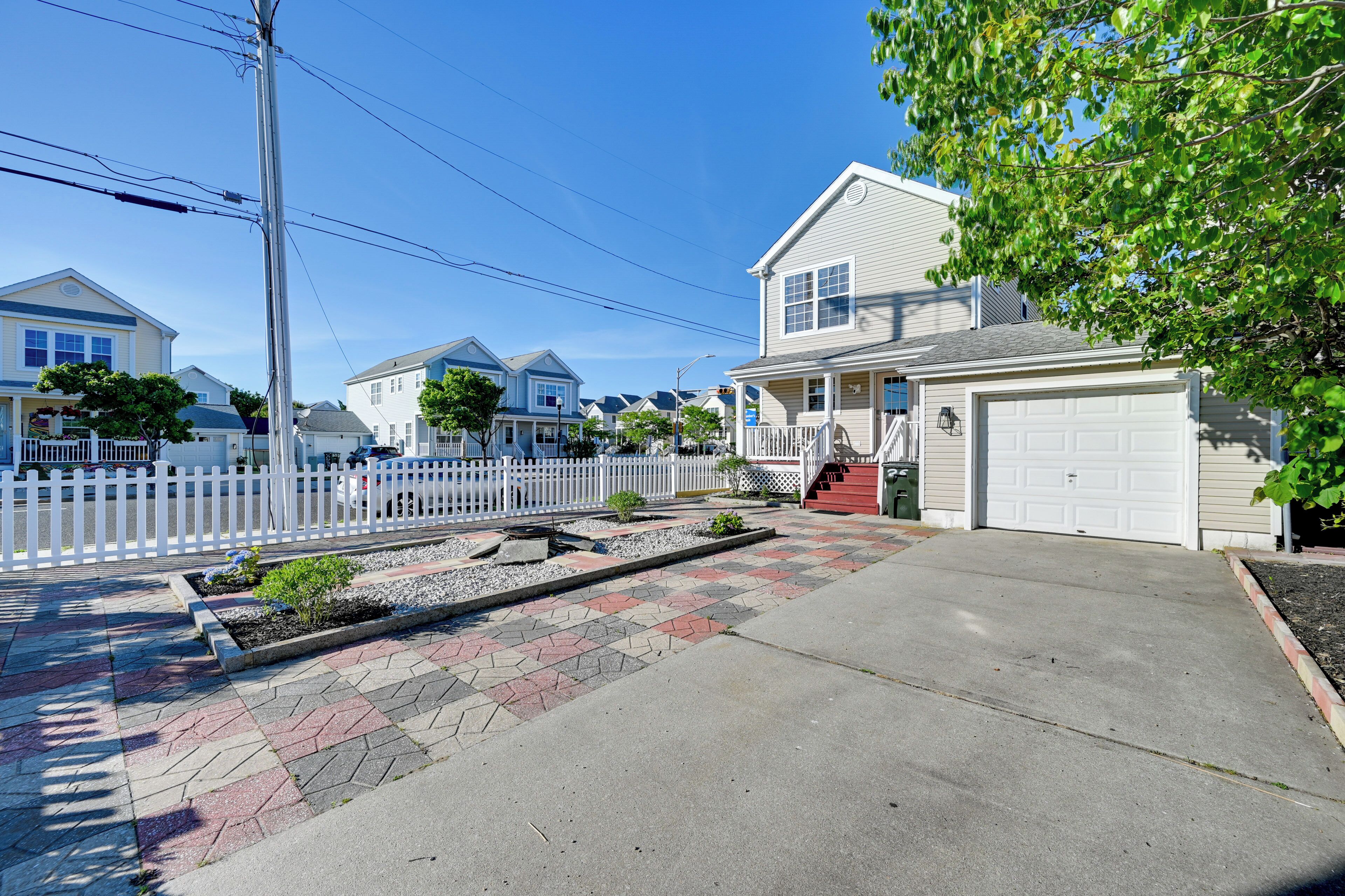 A residential street with houses, a white picket fence, and a garage.