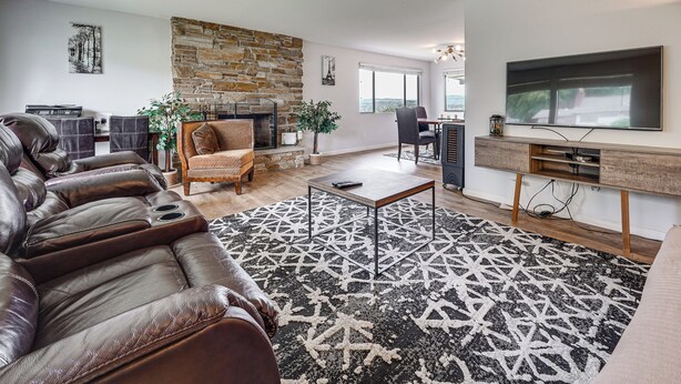 A modern living room with a stone wall, leather sofa, a flat-screen TV, and a fireplace. - Lake View! South End Seattle Home Near Lumen Field (Seattle)