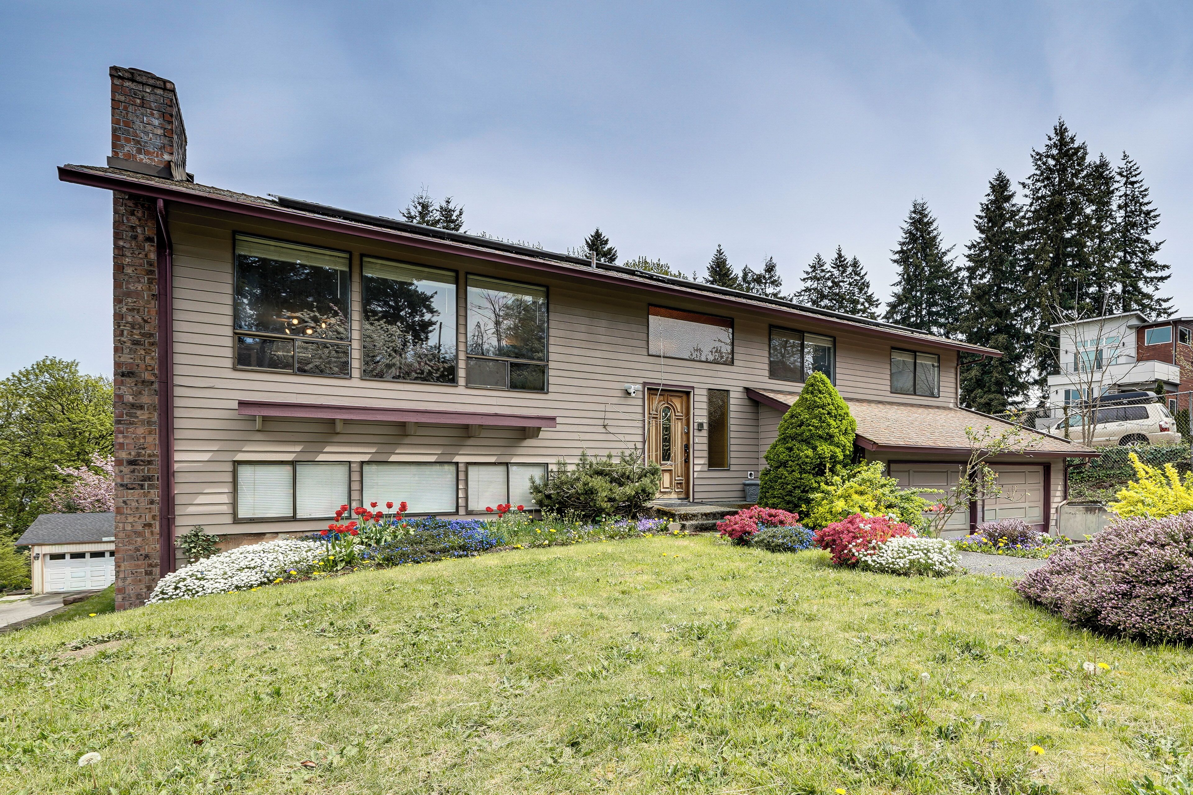 A two-story house with a front porch, a garage, and a well-maintained garden with various plants and flowers.