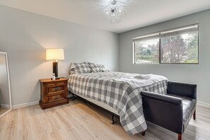 A bedroom with a bed, a nightstand, a chair, a lamp, and a window with a view. - Lake View! South End Seattle Home Near Lumen Field (Seattle)