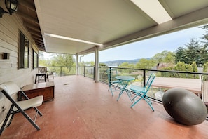Eine überdachte Terrasse mit Blick auf einen See und Hügel, Holzmöbel und ein großer Trainingsball.