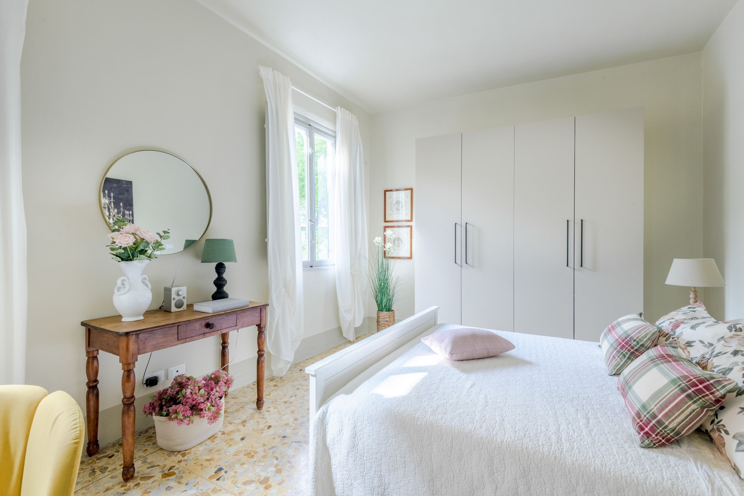 Une chambre à coucher comprenant un lit, des tables de chevet, une commode, un miroir et une fenêtre avec des rideaux.