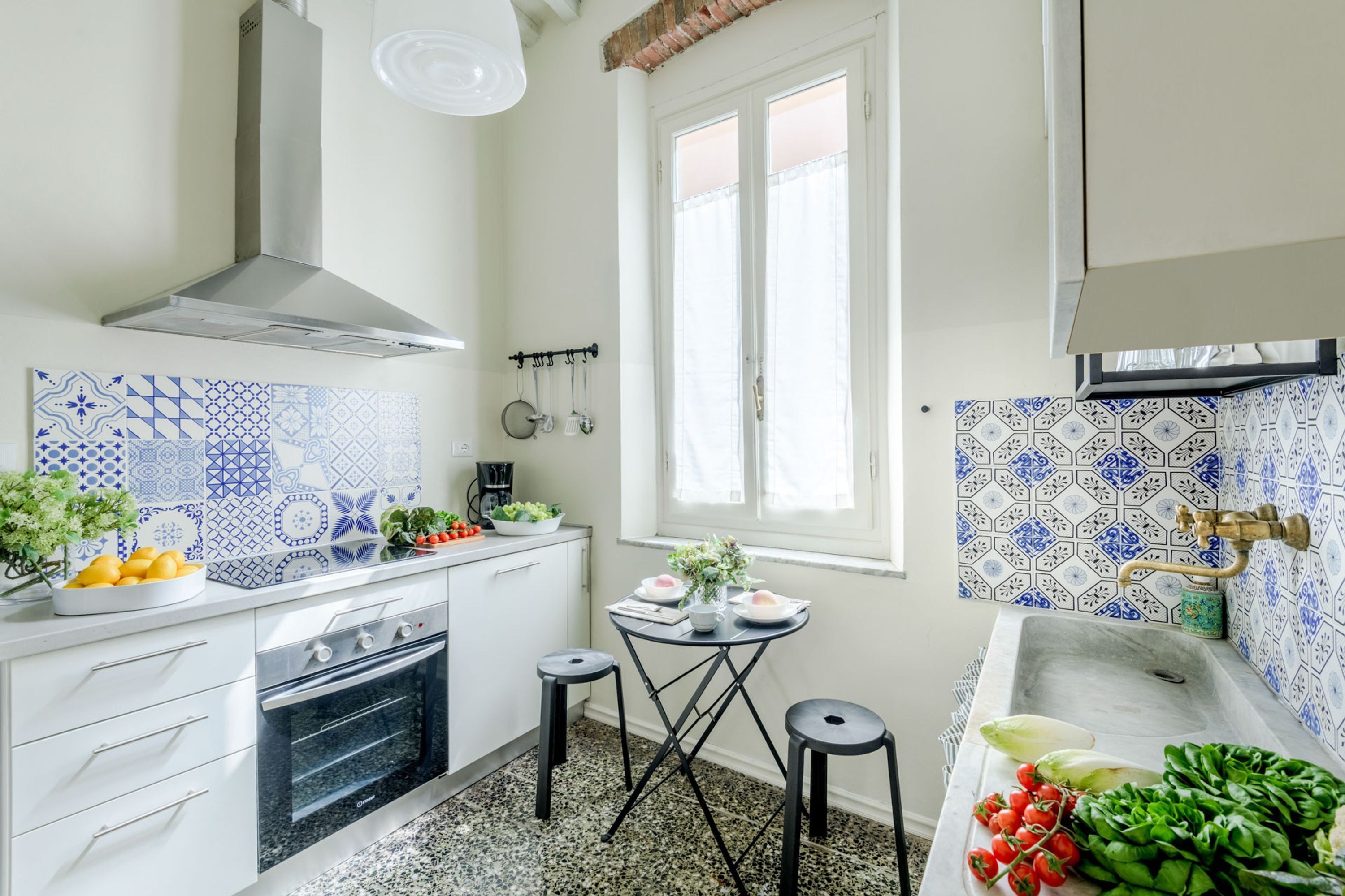 Une cuisine avec des armoires blanches, une cuisinière, un évier et une fenêtre.