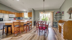 Een keuken met houten kastjes, een centraal eiland, barstoelen en een eettafel met stoelen.