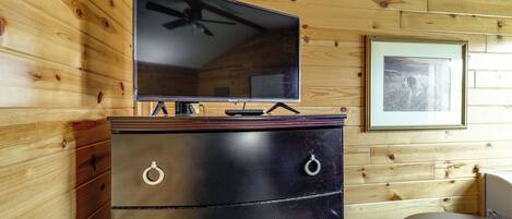Une pièce aux murs lambrissés, avec une télévision posée sur une commode, un tableau encadré accroché au mur et une table à manger.