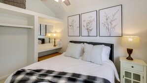 Quarto com cama, ventoinha no teto, obra de arte na parede, abajur e mesa de cabeceira.