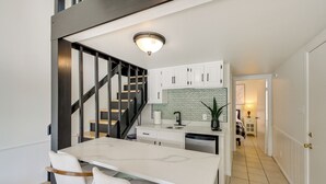 Uma cozinha moderna com armários brancos, uma ilha central e uma escada para um andar superior.