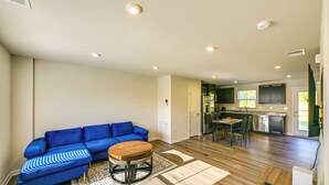 Un salon avec un canapé bleu, une table basse en bois et une cuisine en arrière-plan.