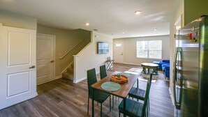 Un vaste espace de vie comprenant une table à manger en bois, des chaises vertes, un canapé et un escalier menant à un autre niveau.