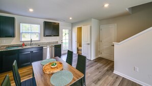 Une cuisine moderne avec des meubles de couleur sombre, une table à manger en bois et une vue sur l’extérieur.