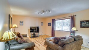 Ein Wohnzimmer mit Fernseher, zwei Sofas, einem Couchtisch und einem Fenster mit Vorhängen.