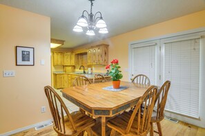 Un coin repas avec une table et des chaises en bois, une plante en pot et une cuisine en arrière-plan.