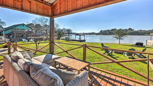 A covered outdoor seating area with wicker furniture, a wooden deck, and a view of a lake and distant buildings. - 3 Cabins on Lake Conroe: Fish, Swim & Explore! (Willis)