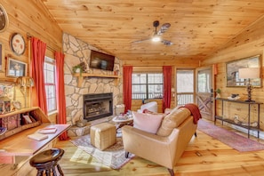 A cozy cabin interior with a stone fireplace, wooden walls, a leather sofa, and a television mounted on the wall. - Private Hot Tub! Book-Lovers' Blue Ridge Retreat (Blue Ridge)