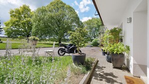 A paved outdoor area with a motorcycle parked, potted plants, and a white building with a door. - Apartment on an Equestrian Estate in Gomadingen (Gomadingen)