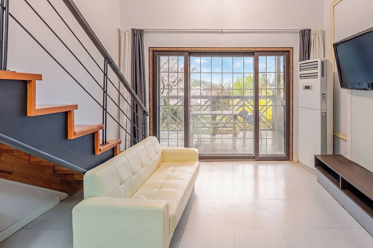 Una sala de estar moderna con sofá, televisor de pantalla plana, escalera y puerta corrediza de vidrio que da a un área exterior.
