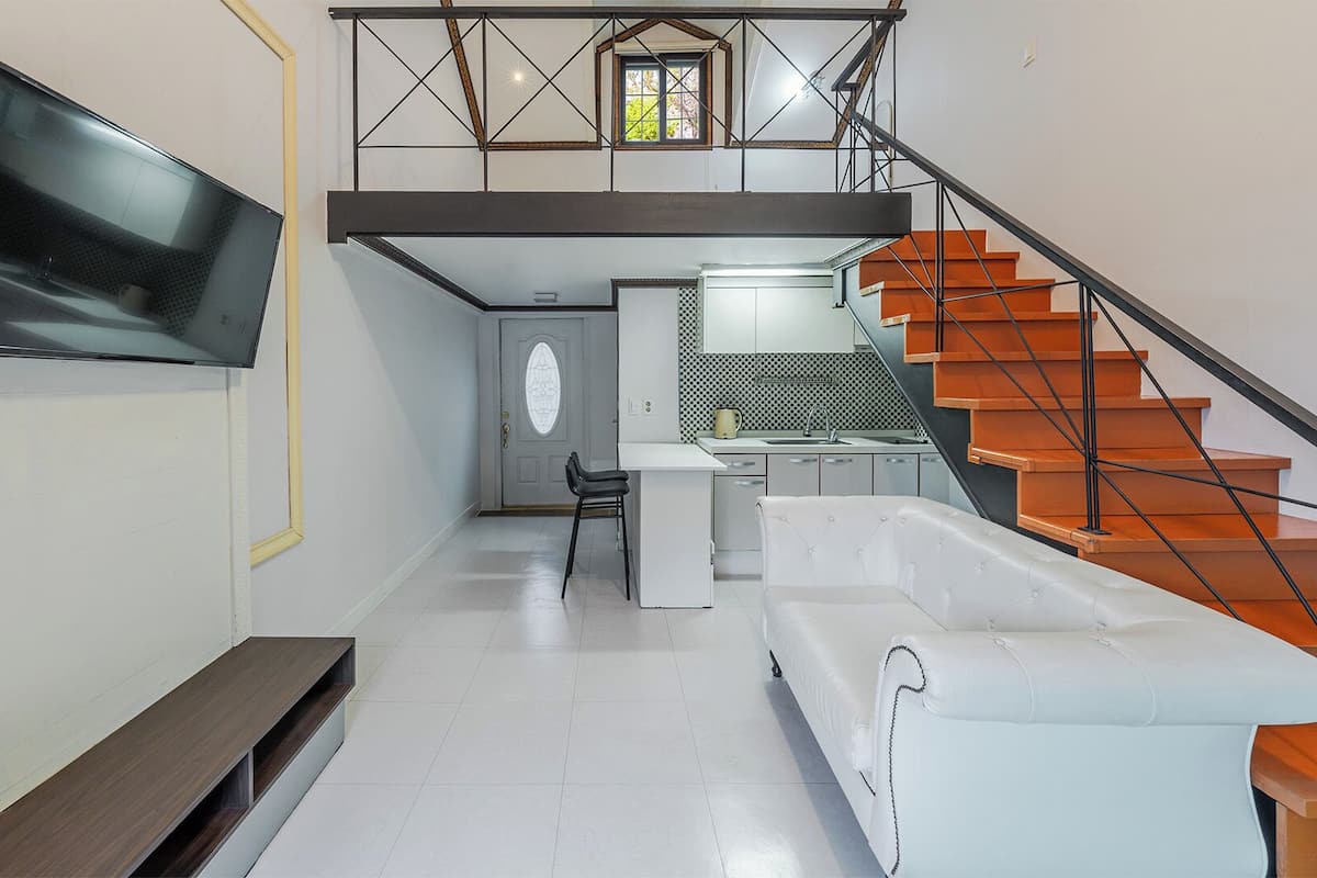 Un interior moderno con una escalera, un televisor de pantalla plana en la pared, una zona de cocina y un área de estar.
