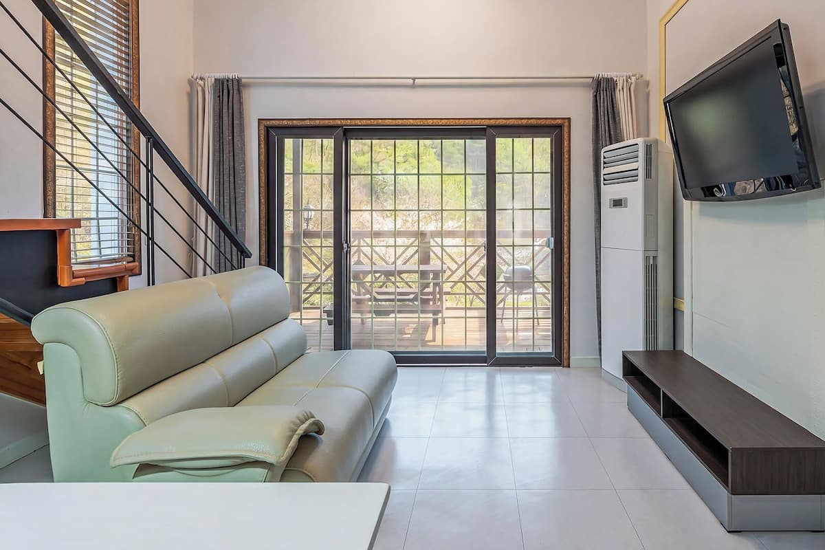 Una sala de estar con un sofá, un televisor montado en la pared, un ventanal corredizo que da a un patio exterior y una escalera.