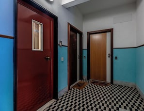 Ein Korridor mit Schachbrettfußboden, einer roten Tür mit Fenster und einer Holztür.