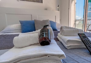 Siististi pedattu sänky, jonka päällä on pullo shampoota, pino taiteltuja pyyhkeitä ja kaukosäädin.