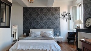 Un dormitorio con cama, mesitas de noche, una silla, lámpara, reloj y un adorno en la pared.