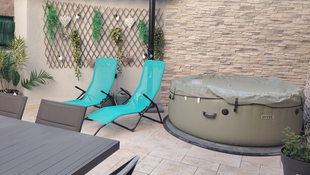 Un patio con dos sillones turquesa, un jacuzzi redondo y una mesa.