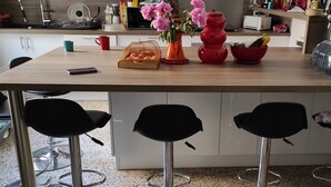 Una cocina con mostrador de madera, cuatro taburetes negros, un jarrón rojo con flores, un tazón rojo y una botella de agua.