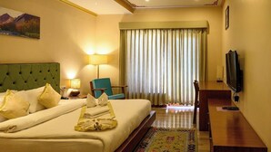Ein Hotelzimmer mit Bett, Sessel, Fernseher, Schreibtisch und einem fensterbepflanzten Fenster.