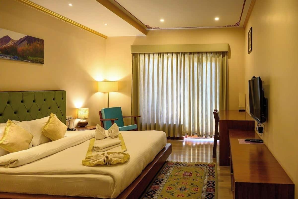A hotel room with a bed, a chair, a television, a desk, and a window with curtains.