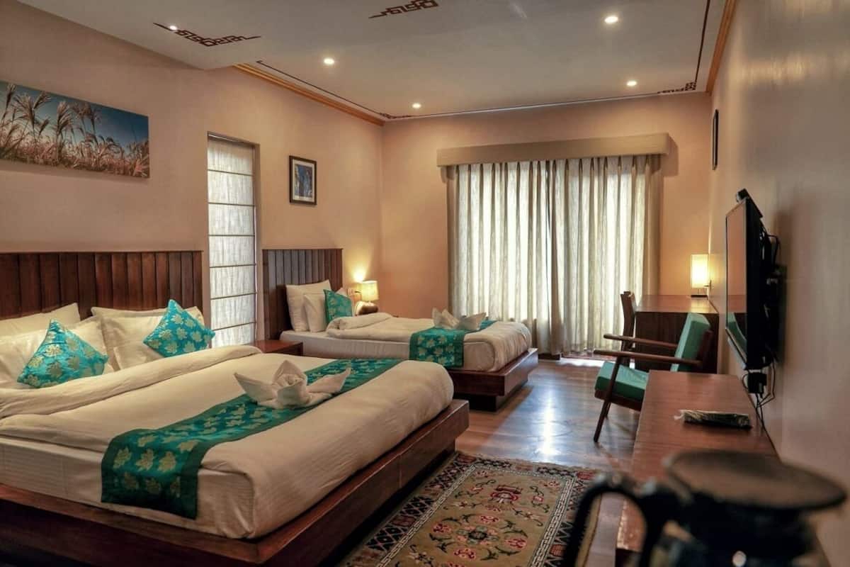 A hotel room with two beds, a desk, a chair, a television, and a window with curtains.