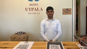 Ein Hotelrezeptionstresen mit einem Logo, ein Mann steht dahinter und auf dem Tisch befindet sich ein QR-Code.