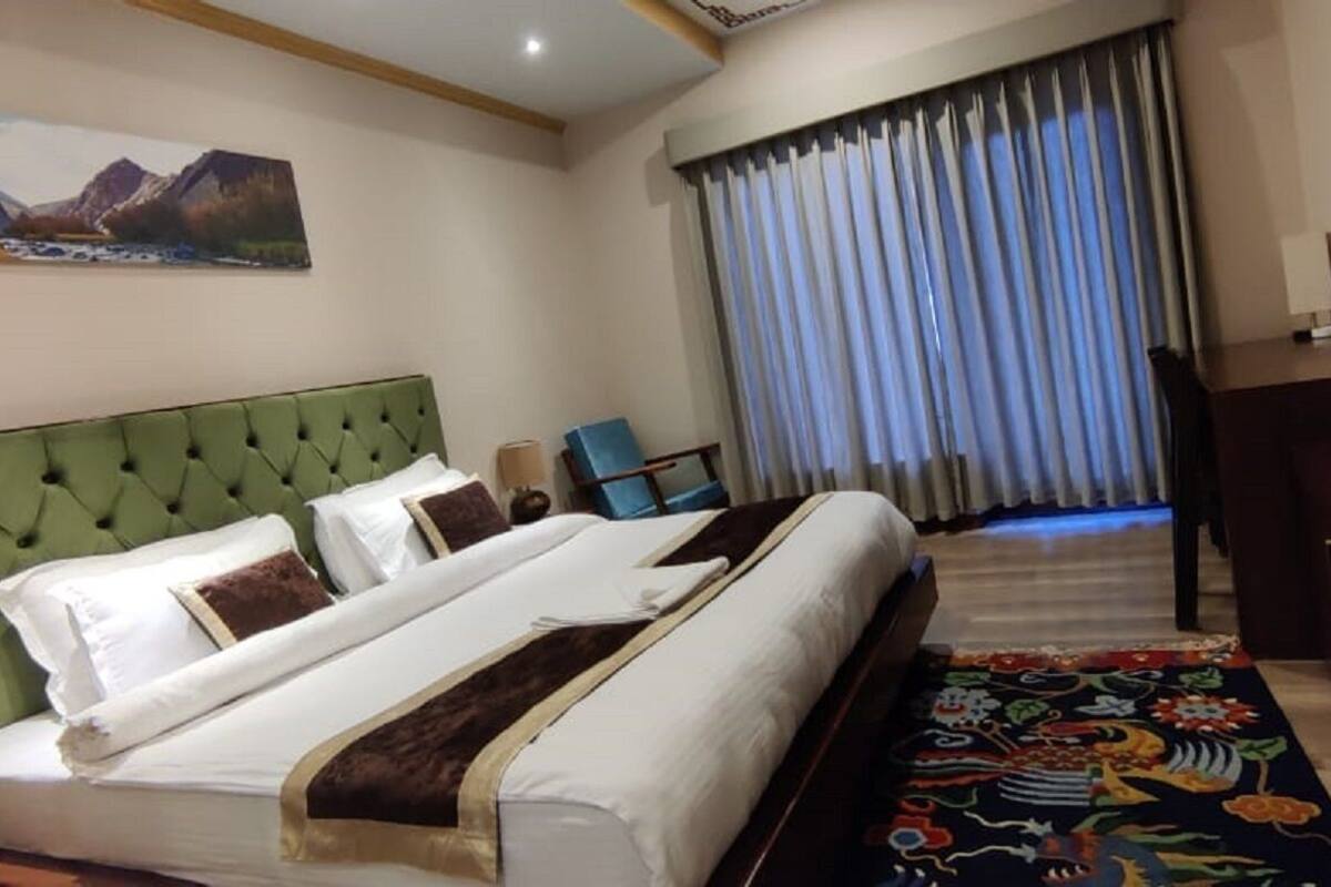 A hotel room with a large bed, a television, a desk, and a window with curtains.