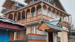 A multi-story house with a balcony, a chimney, and a small attached structure. - Not just a stay, a peaceful escape into nature.” (Bali Chowki)