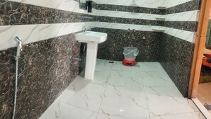 A bathroom with a sink, shower, and a red container on the floor. - Not just a stay, a peaceful escape into nature.” (Bali Chowki)
