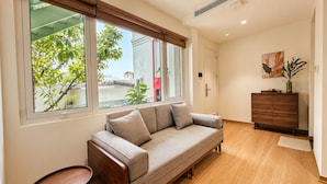 Una sala moderna con un sofá, un mueble de madera y un ventanal con vistas a zonas verdes.