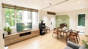 A modern living room with a TV, dining table, chairs, and a kitchen area. - Joy Apartment Pearl West Lake (Tay Ho)