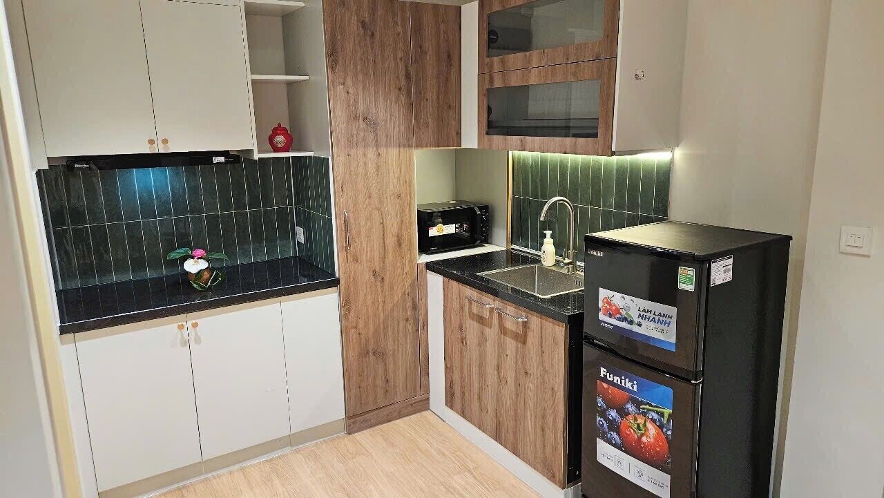 Una cocina con encimera negra, armarios de madera, microondas, refrigerador y pileta.